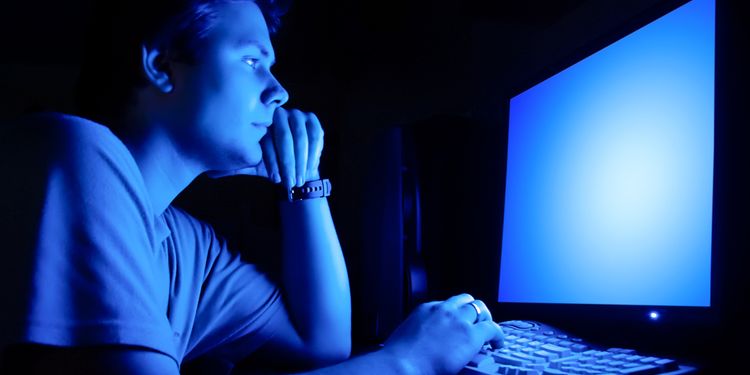 Photo of a man staring at the blue screen in dark room