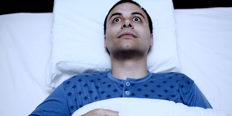 Insomniac man lying in bed with eyes wide open