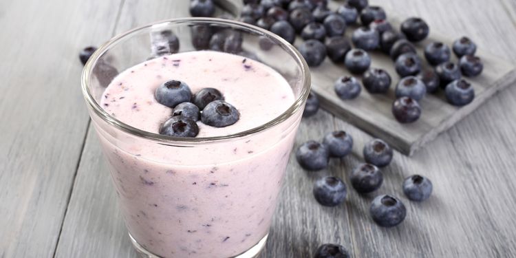 Photo of blueberry yogurt smoothie in a glass with blueberries around