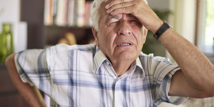 Photo of an old man holding his head in pain