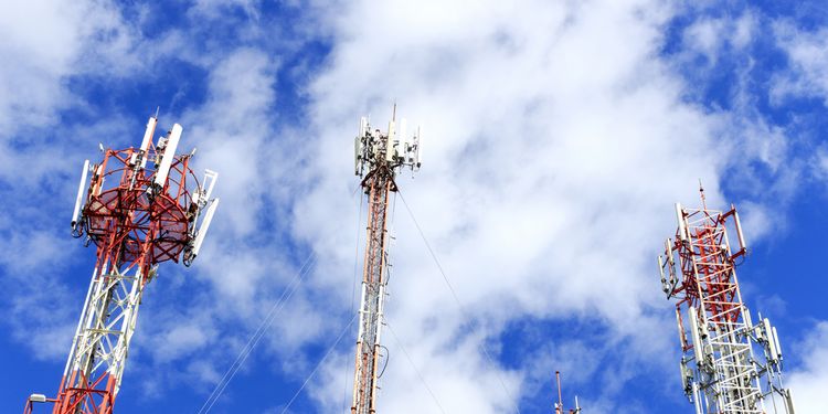 Photo of cell phone and communication towers against blue sky