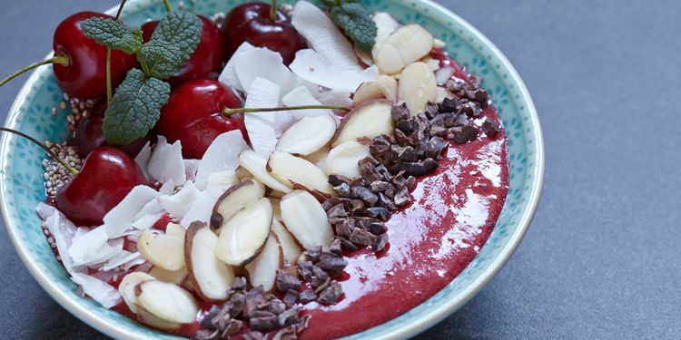 Photo of a cherry almong smoothie in a bowl topped with almond chips and cherries