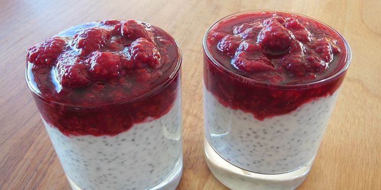 Photo of two glasses with yoghurt and chia seed and raspberry on top