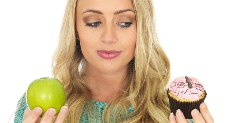 Photo of a woman undecided what to eat - apple or a cake