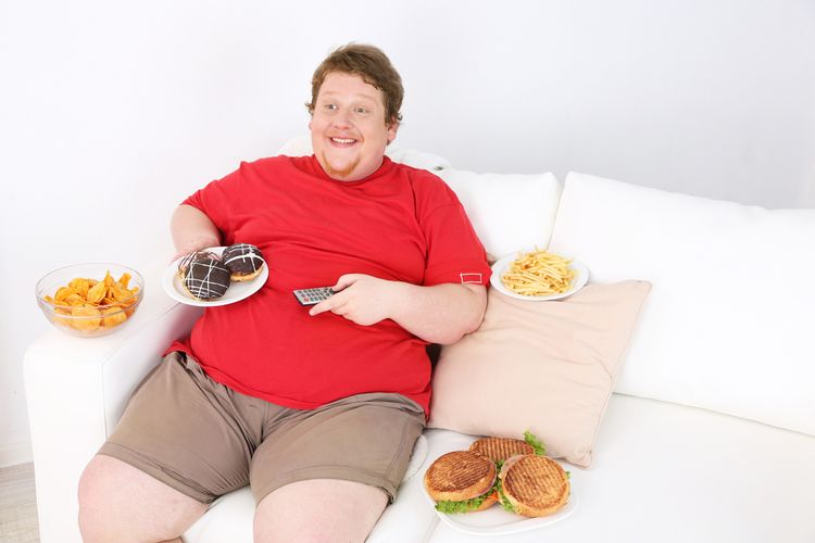 Photo of a Lazy overweight male sitting with fast food on couch and watching television