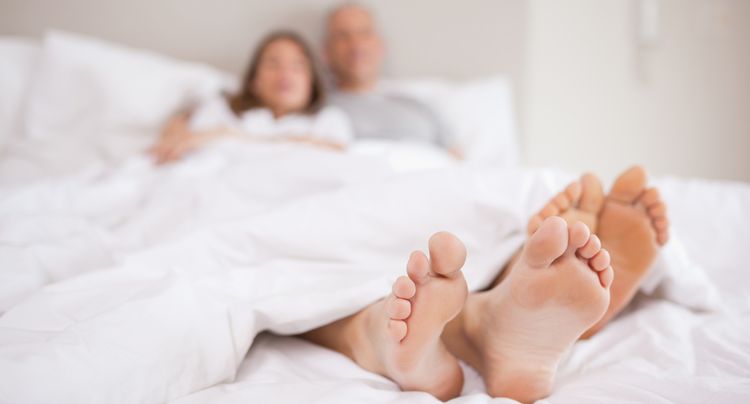 Photo of couple lying in a bed with the camera focus on their feet