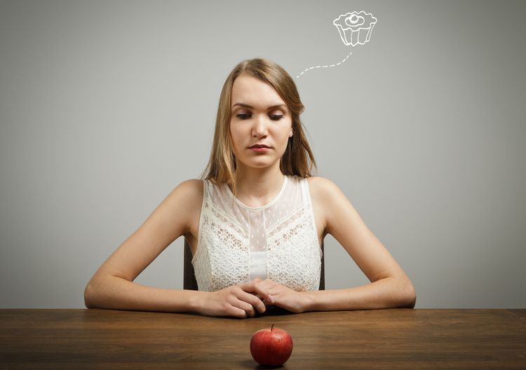 Photo of a woman thinking on cake looking at an apple