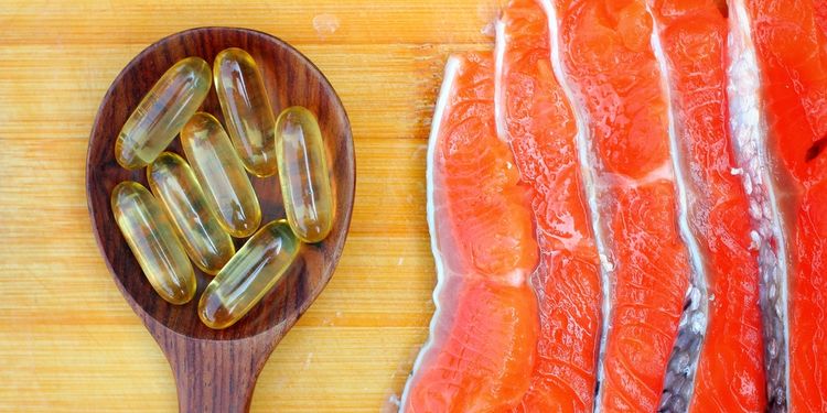 Photo of fish oil caps in a spoon next to fish filet 