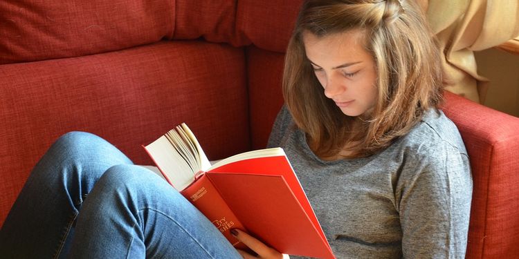 Photo of a girl sitting on a couch reading a red book