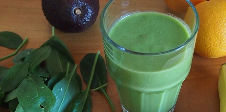 Photo of spinach smoothie in a glass with spinach leaves next to it