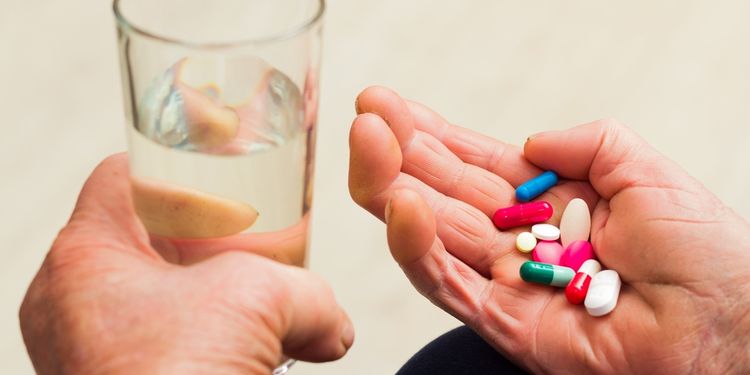 Photo of an old persons hand holding glass of water and pills