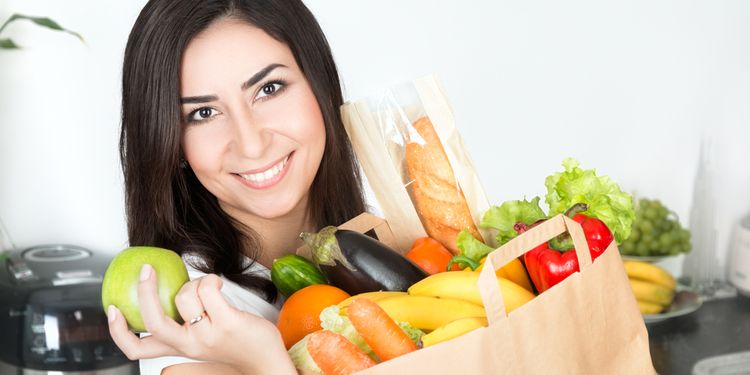 Photo of a young woman smiling and holding bag of vegetables