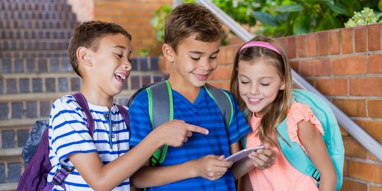 Photo of happy school kids looking at mobile phone at school