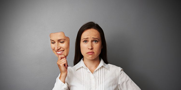 Photo of a sad woman taking off her happy face mask