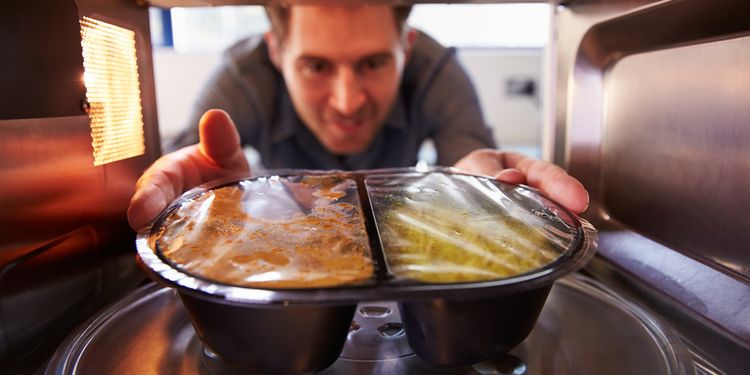 Photo of a man pulling out the dish with food from microwave oven