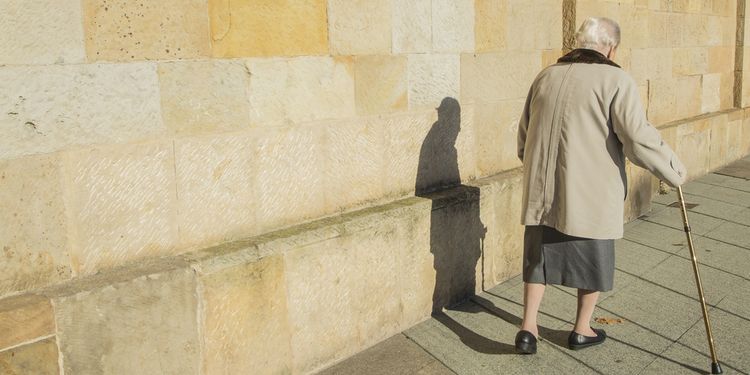 Photo of an old woman with a cane walking in street