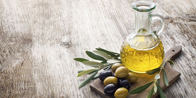 Olive oil with raw olives on table