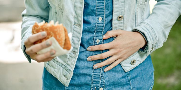 Photo of woman eating burger and holding her stomach in pain