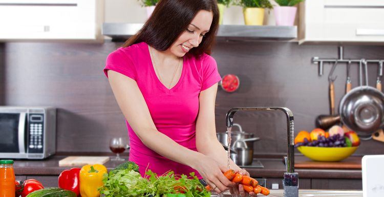 Photo of young woman washes the vegetables in domestic kitchen