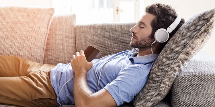 Photo of a man lying on couch listening relaxing music