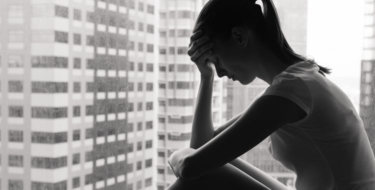 Black and white photo of sad and lonely woman in the city sitting next to a window