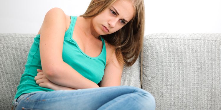 Photo of woman having abdominal pain sitting on couch