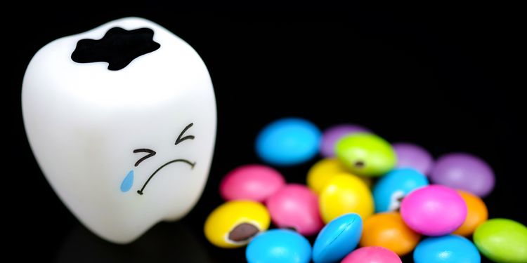 Photo of a plastic tooth toy crying next to pile of sugary candies