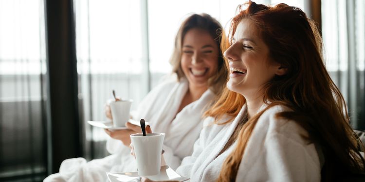 Photo of happy women in bathrobes enjoying tea during wellness weekend