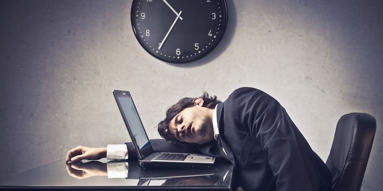 Photo of tired businessman sleeping on a laptop with clock in the background