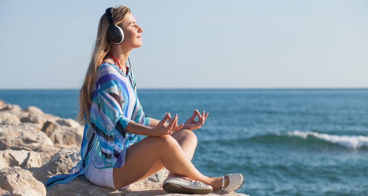 Photo of a woman meditating on a sea coast and listening music through headset